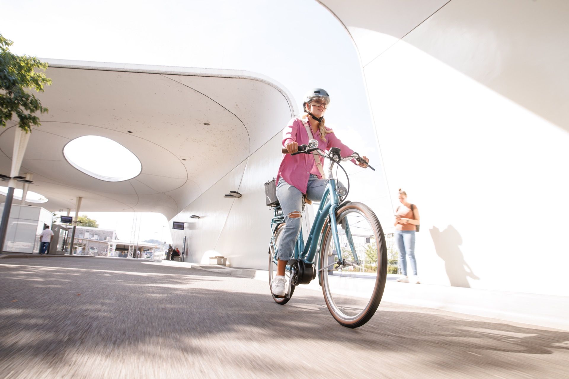 A girl wearing a pink blouse rides her bike through a modern city.